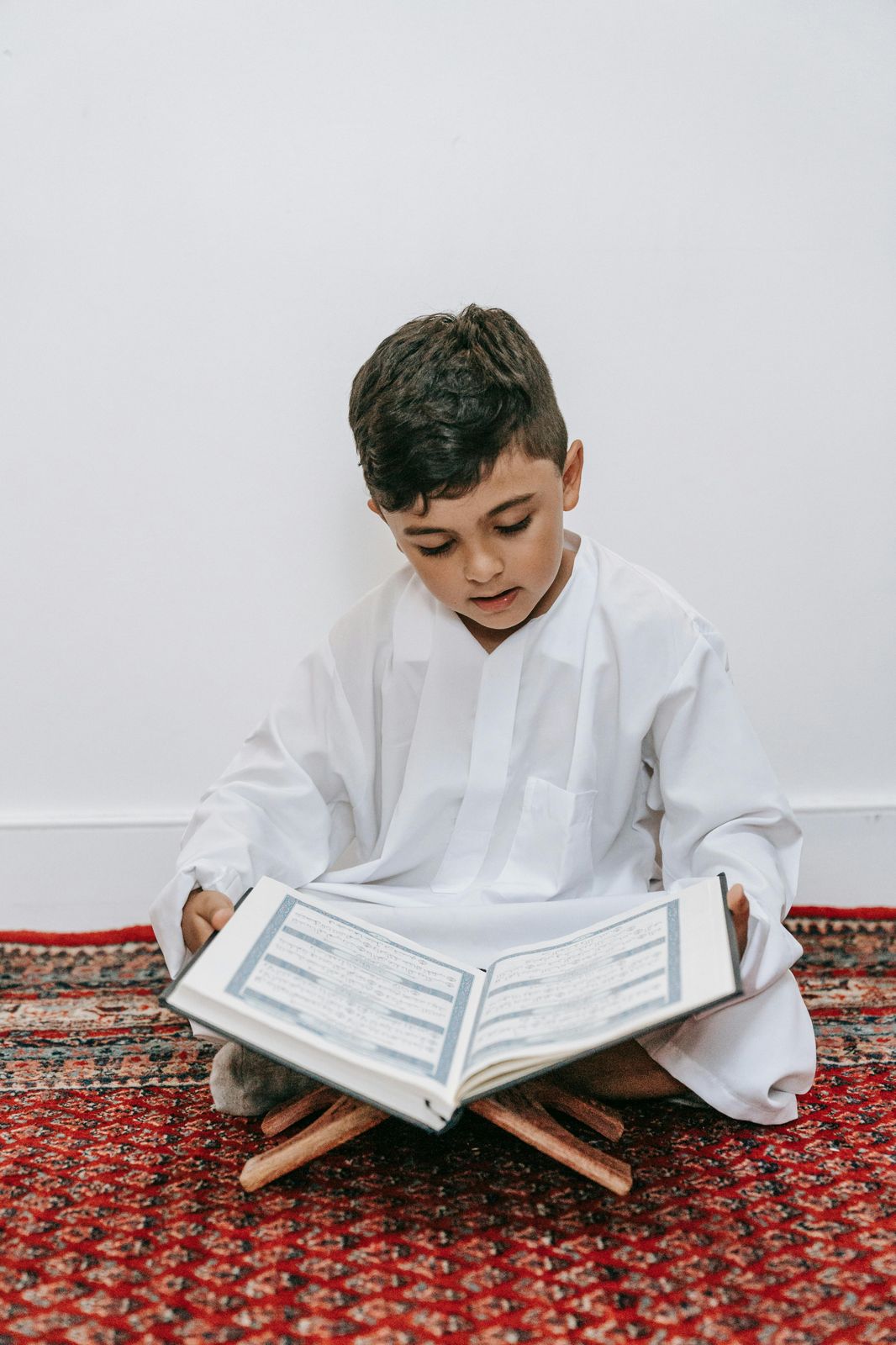 Boy reading the Quran from a wooden stand at home