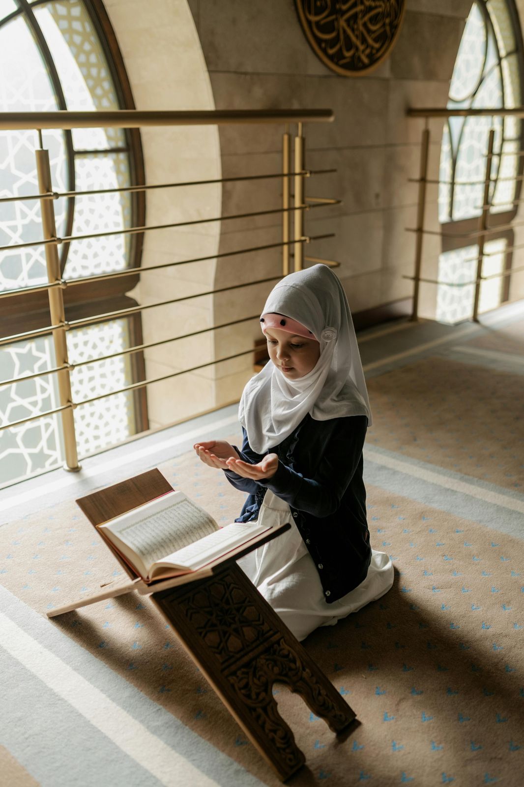 Young girl making dua beside the Quran in a mosque